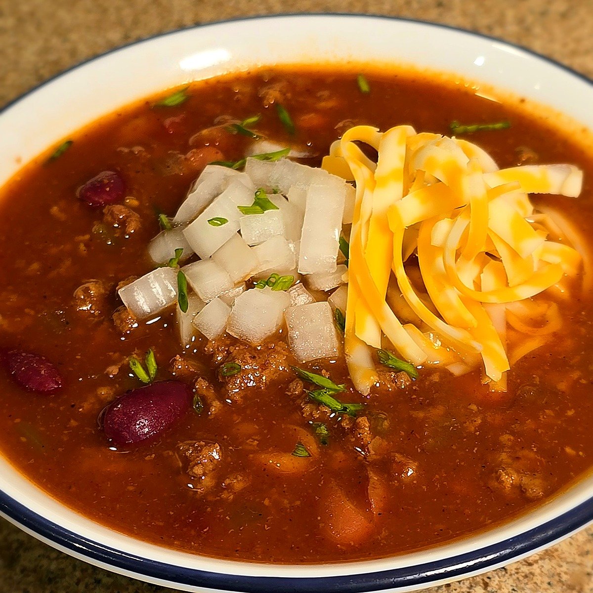 Bowl of copycat Wendy's chili topped with shredded cheese and diced onion