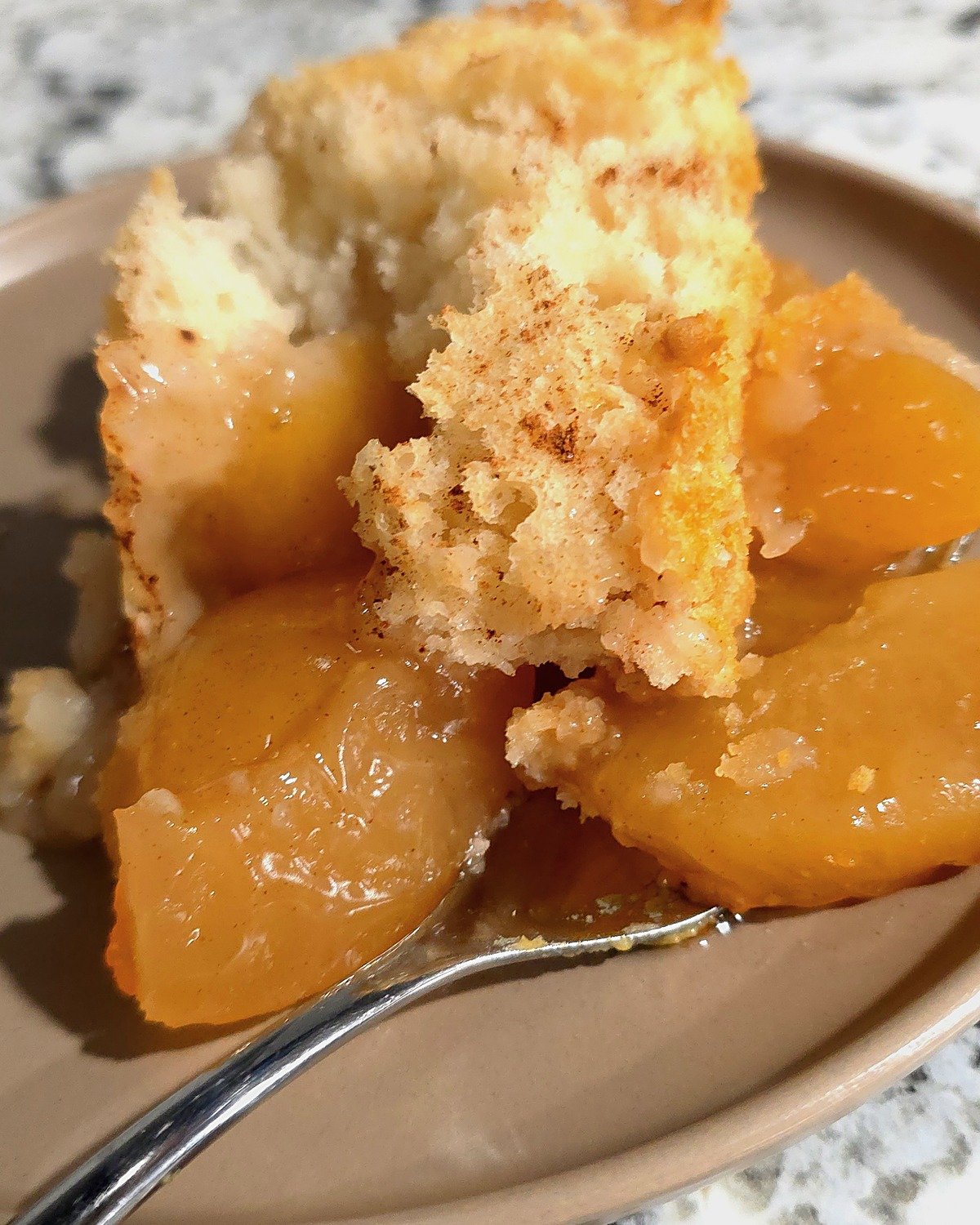 Apple cinnamon dump cake on a plate with a fork, soft cake over glossy apple pie filling