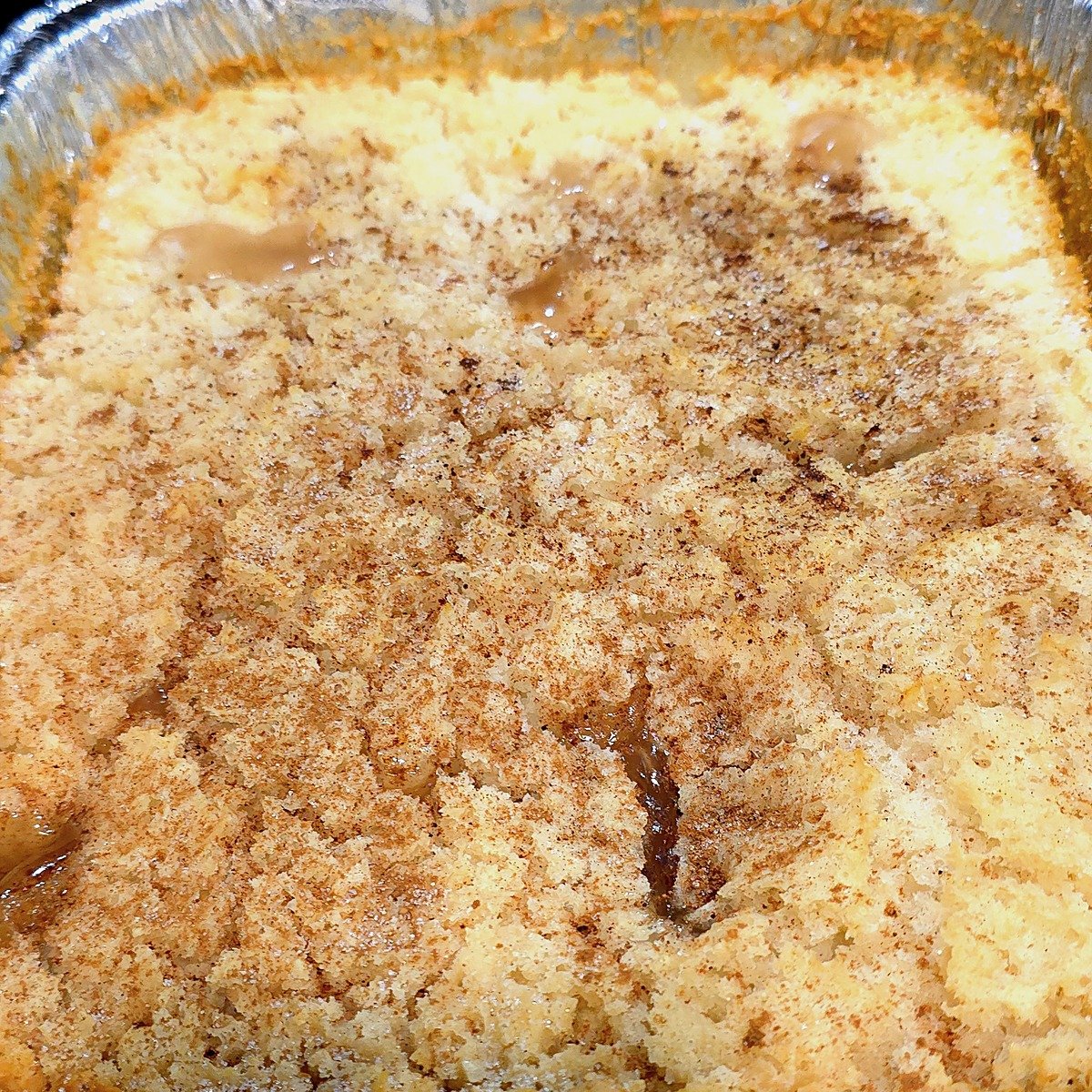 Apple cinnamon dump cake in a foil pan with cinnamon dusted on top