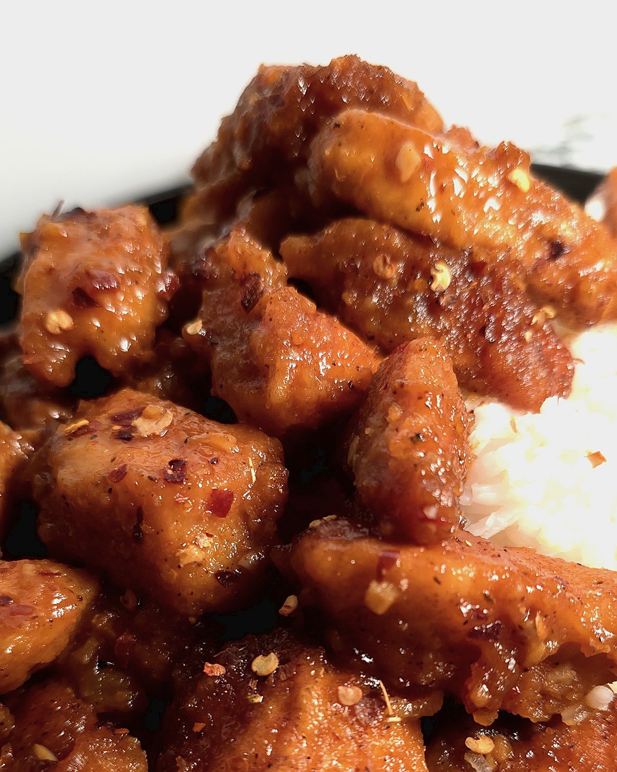 Close-up of crispy firecracker chicken pieces with sticky glaze over rice