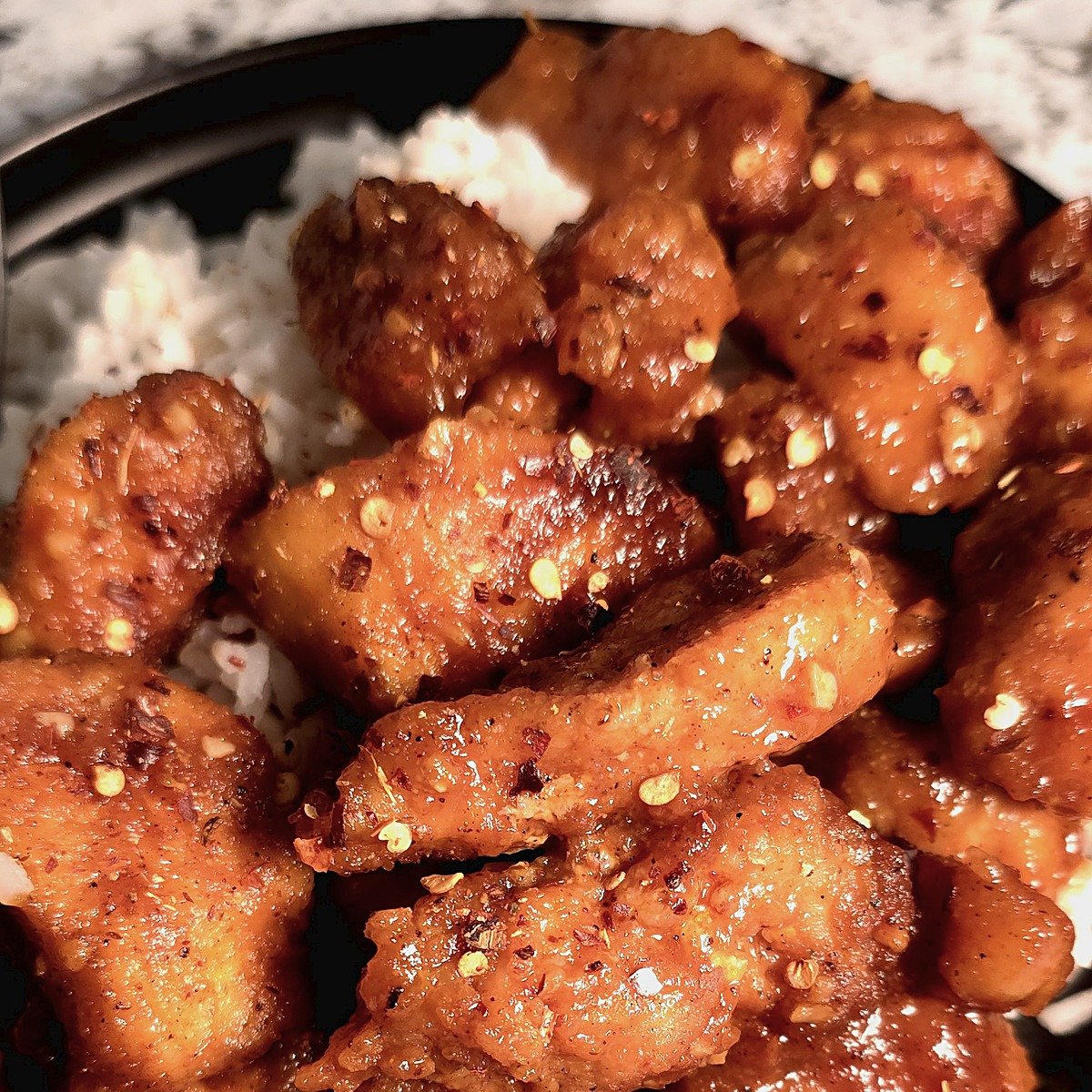 Firecracker chicken over rice on a black plate