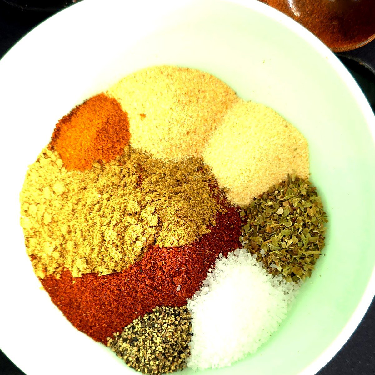 Taco seasoning spices measured into a bowl: chili powder, paprika, cumin, garlic powder, onion powder, oregano, salt, pepper and cayenne