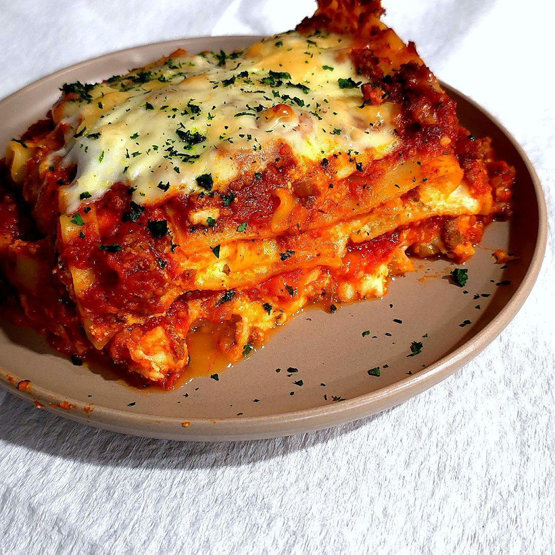 Slice of ultimate spicy sausage lasagna with melted mozzarella and parsley on a plate