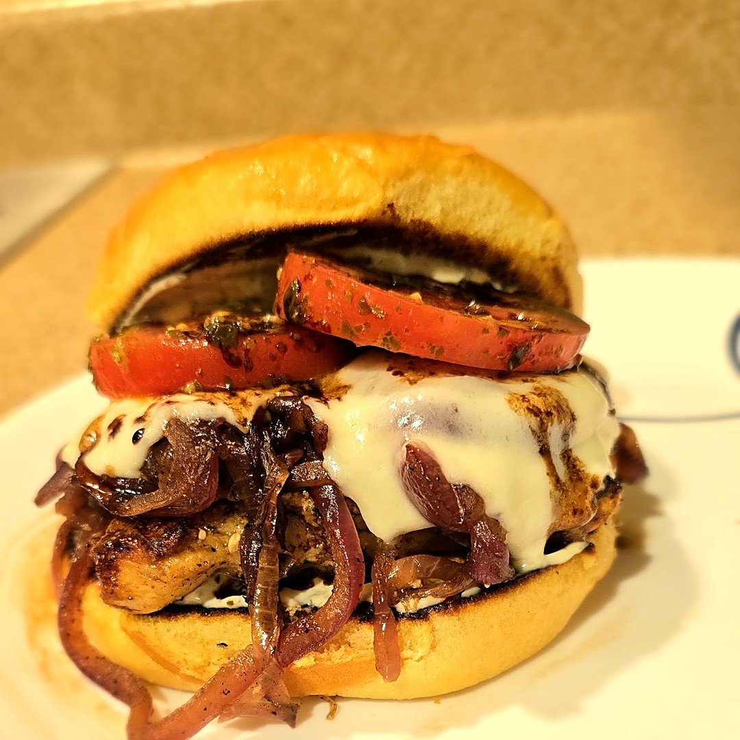 Pesto bruschetta chicken sandwich with caramelized onions, melted mozzarella, and pesto tomatoes on a brioche bun