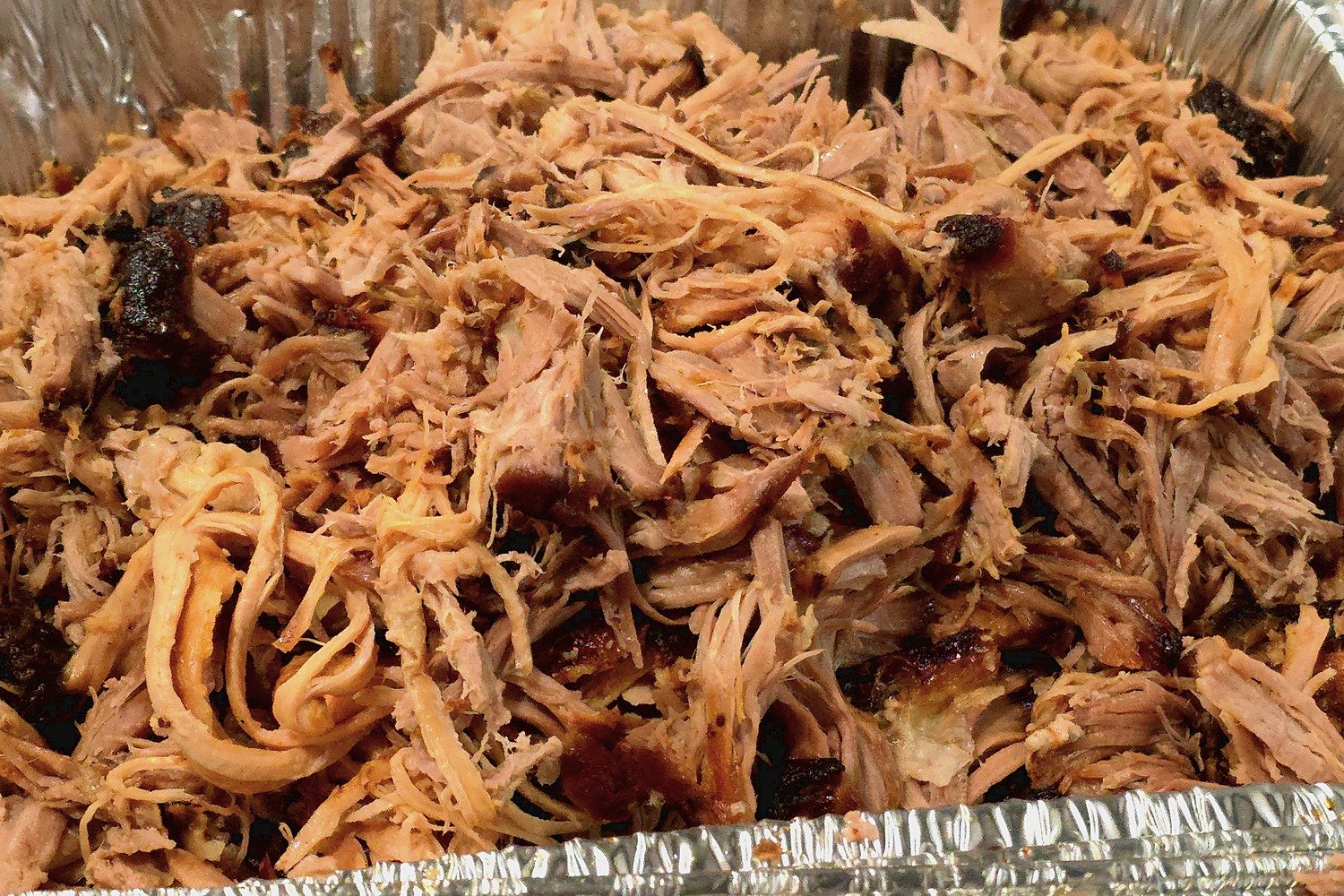 A pan of shredded oven pulled pork with pieces of bark mixed in