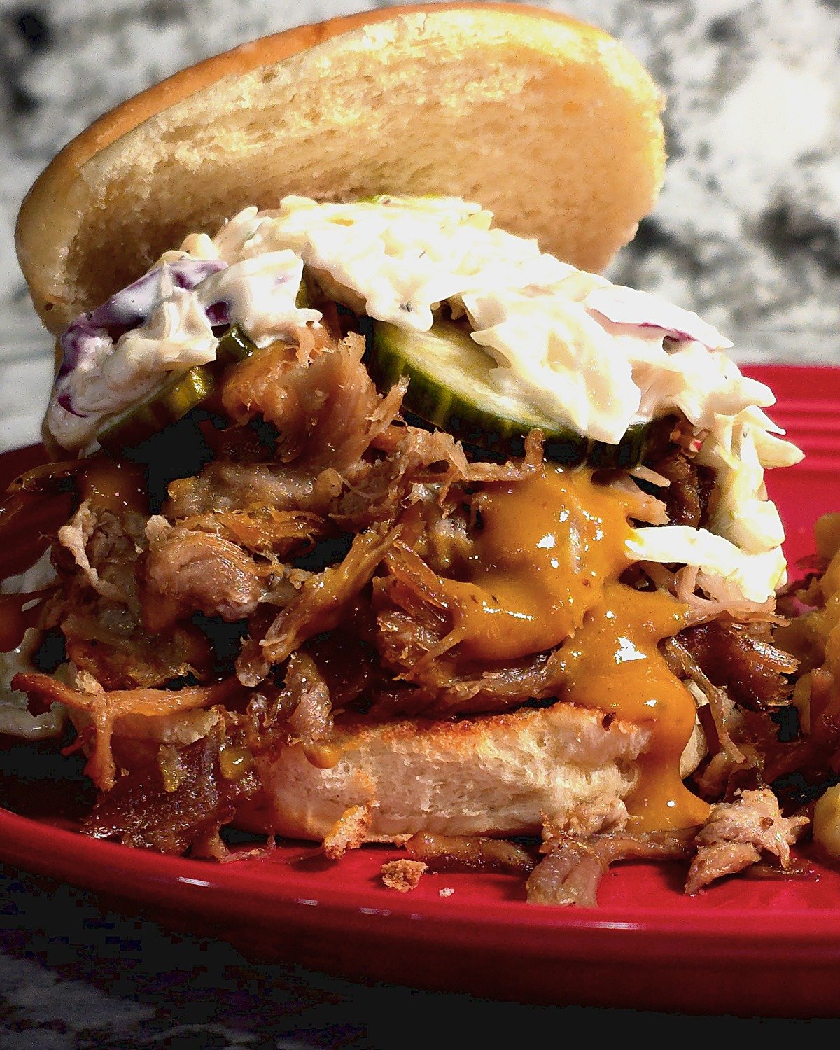 Open-faced pulled pork sandwich with creamy coleslaw, pickle slices and gold BBQ sauce