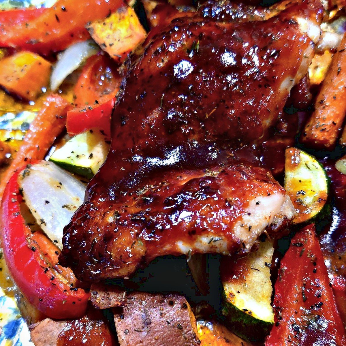Close-up of a sweet heat BBQ glazed chicken thigh with roasted zucchini, red pepper and onion